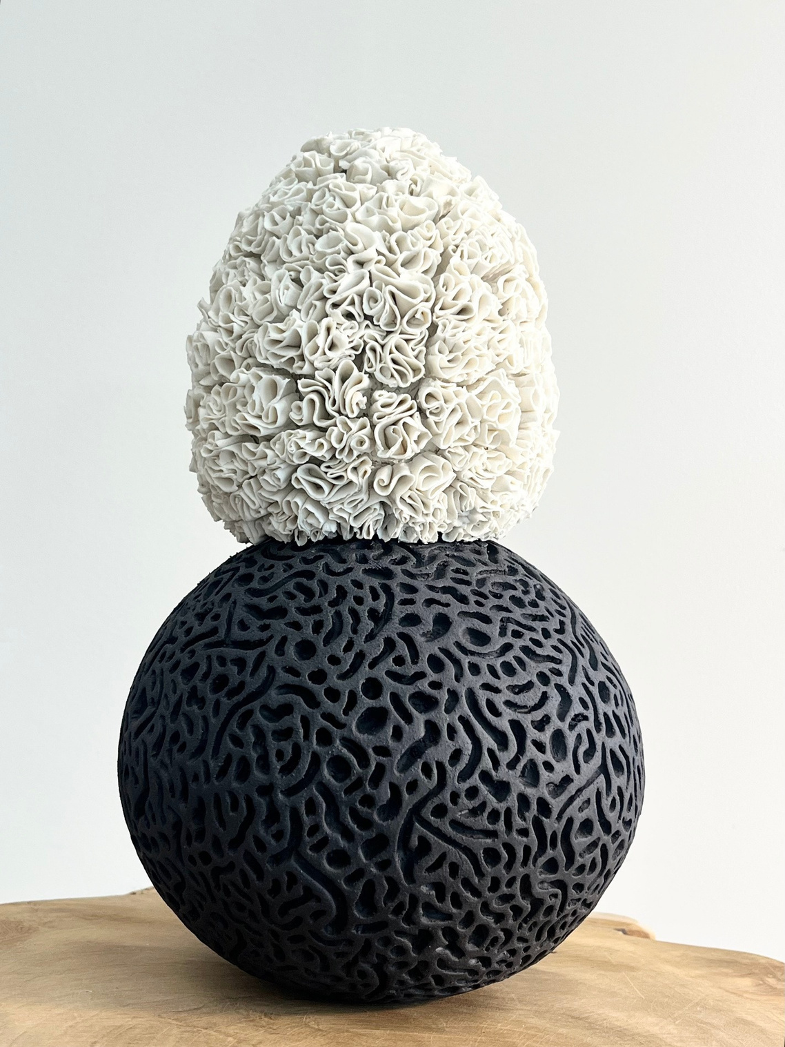 A body that holds both sculpture — white porcelain layered with curled petals on a dark stoneware sphere with coral-like texture — view 2