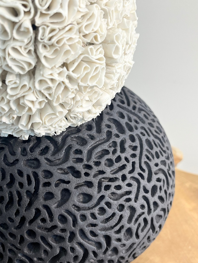 A body that holds both sculpture — white porcelain layered with curled petals on a dark stoneware sphere with coral-like texture — view 3