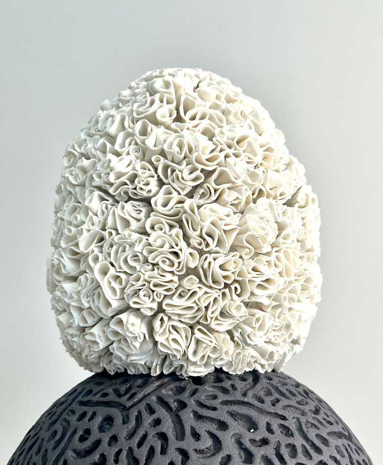 A body that holds both sculpture — white porcelain layered with curled petals on a dark stoneware sphere with coral-like texture