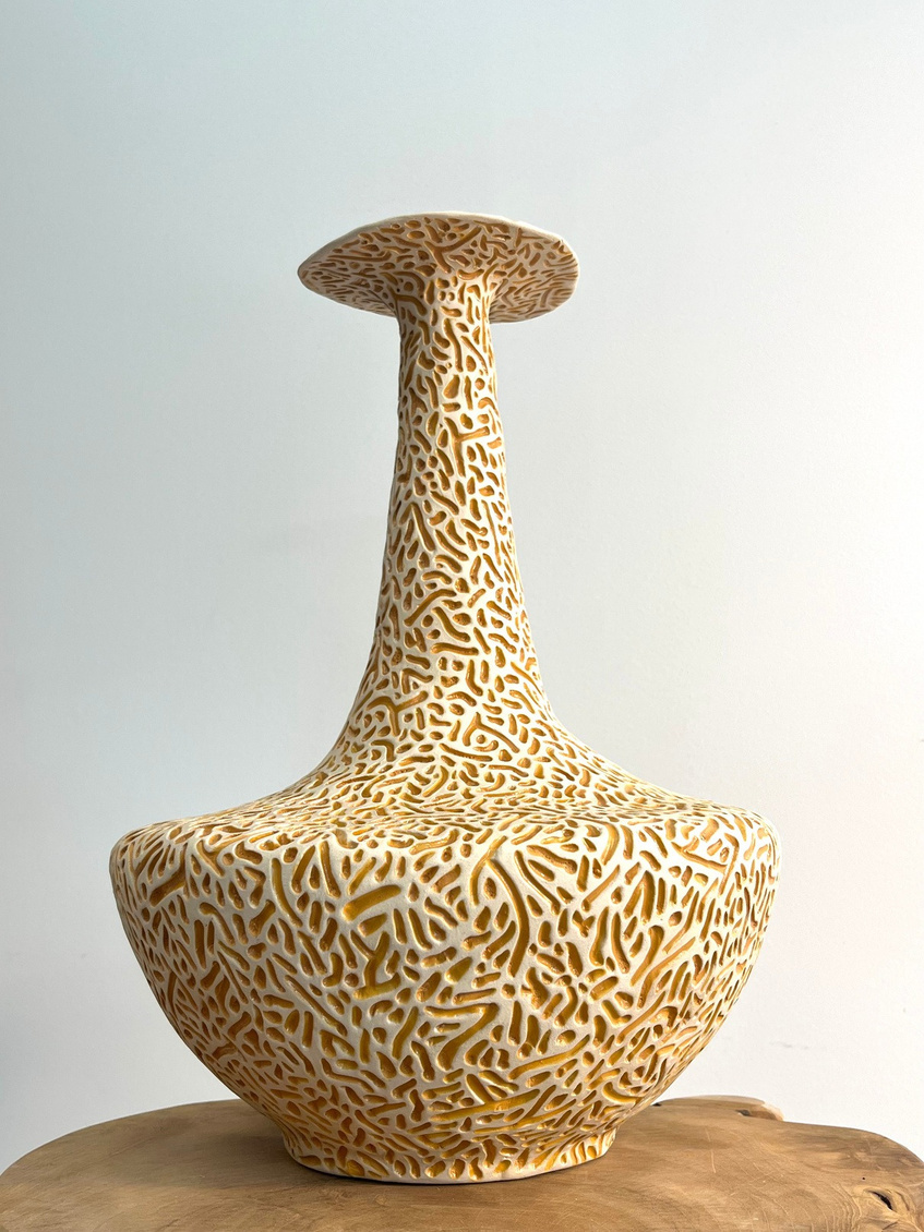 Ambra sculptural vase, tall stoneware with dense carved pattern and warm amber glaze pooling in the grooves