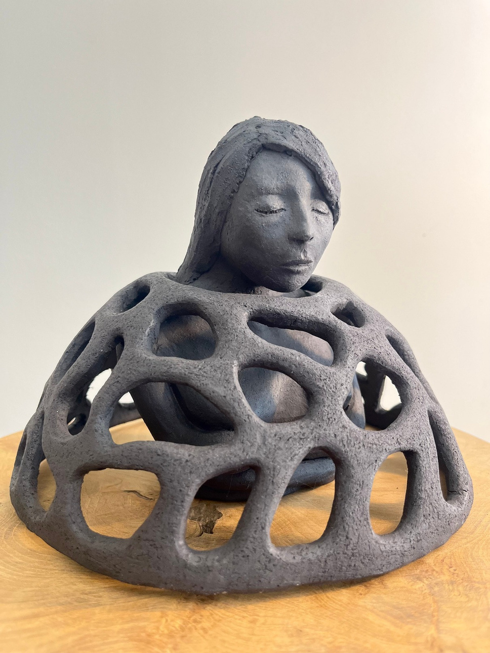 Armour sculpture, dark stoneware figure inside a latticed dome, eyes closed — view 2