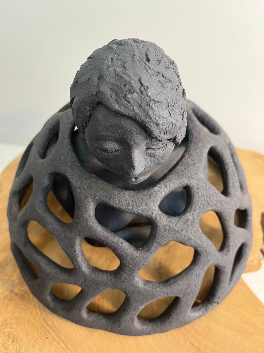 Armour sculpture, dark stoneware figure inside a latticed dome, eyes closed