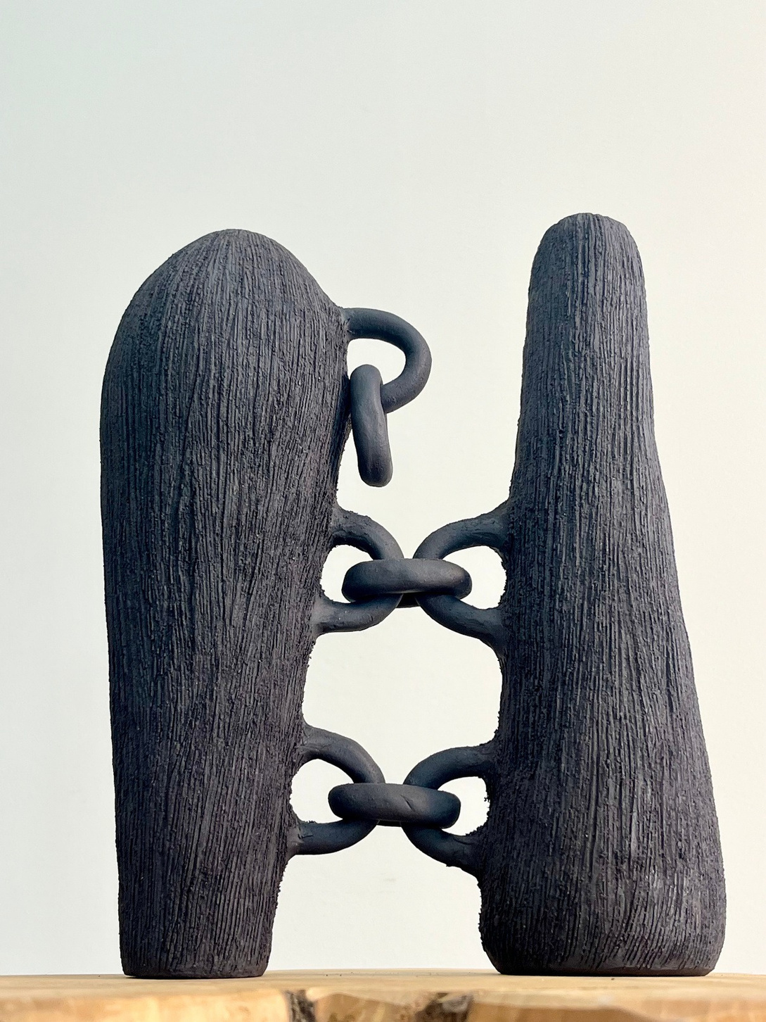 Broken bonds sculpture, two dark stoneware vertical forms connected by hand-rolled clay chains — view 2