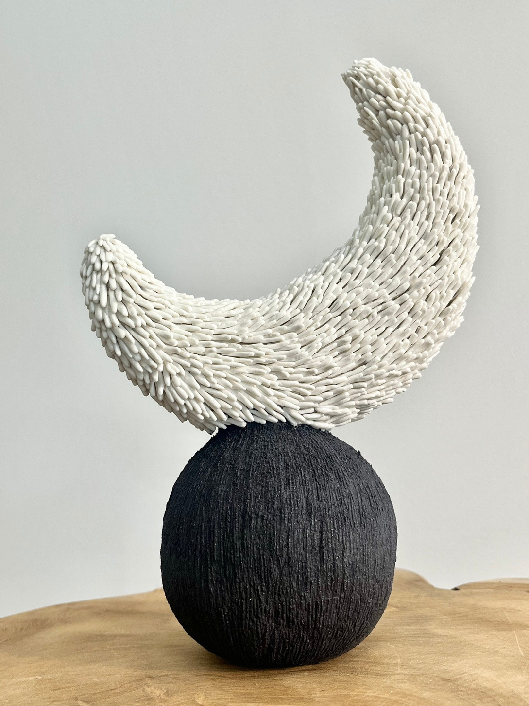 Luna sculpture, crescent of white porcelain with pressed texture resting on a dark stoneware sphere — view 3