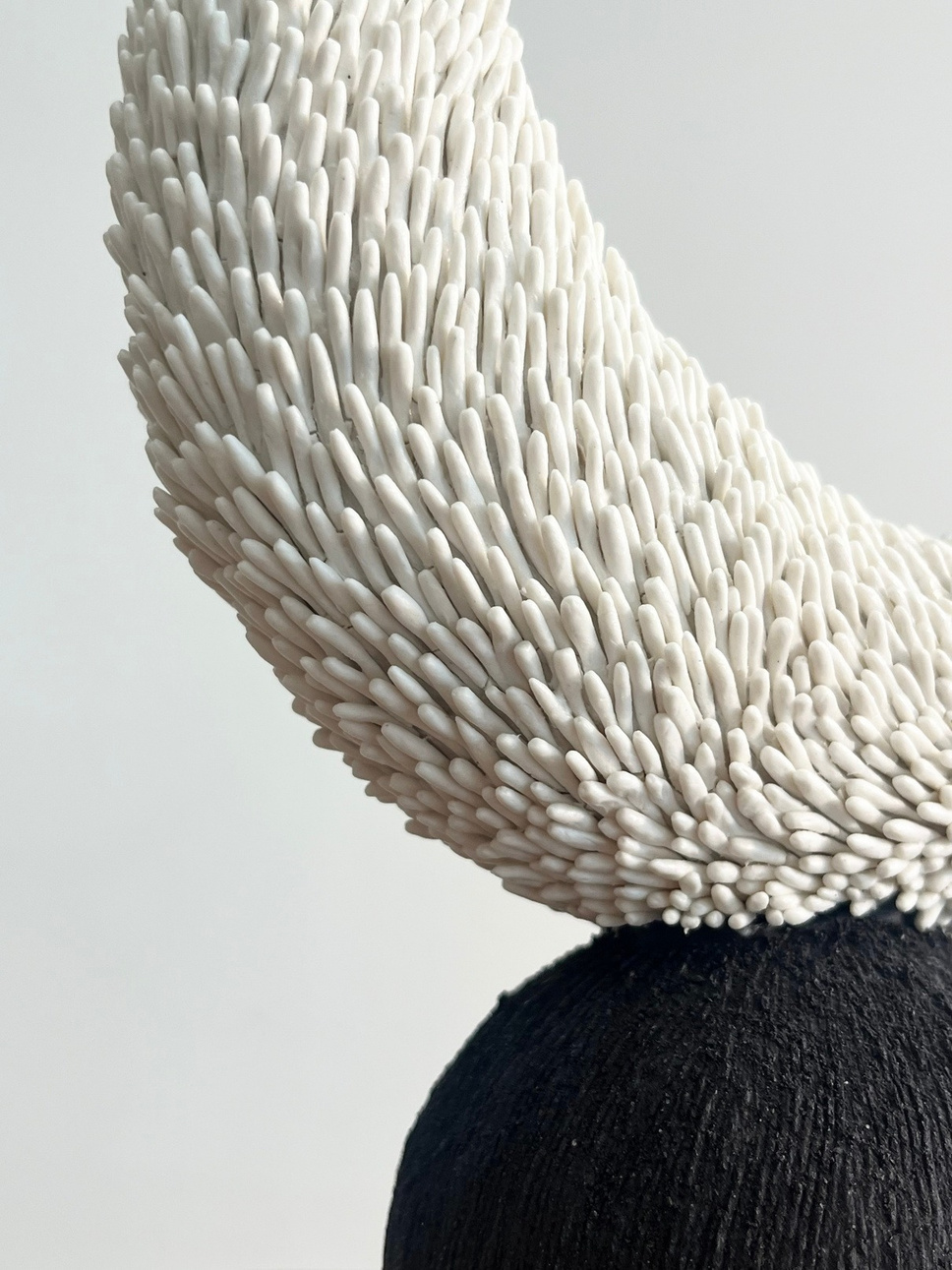 Luna sculpture, crescent of white porcelain with pressed texture resting on a dark stoneware sphere