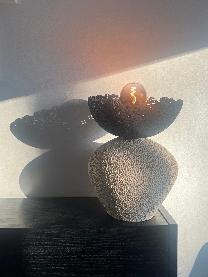 Nyx halo lamp sculpture, dark stoneware perforated bowl balanced on a pale textured sphere, with glowing filament bulb — view 2