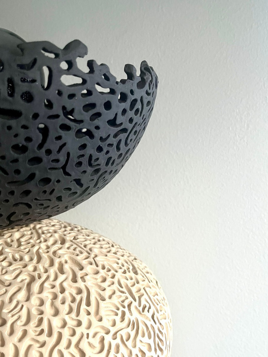 Nyx halo lamp sculpture, dark stoneware perforated bowl balanced on a pale textured sphere, with glowing filament bulb — view 4
