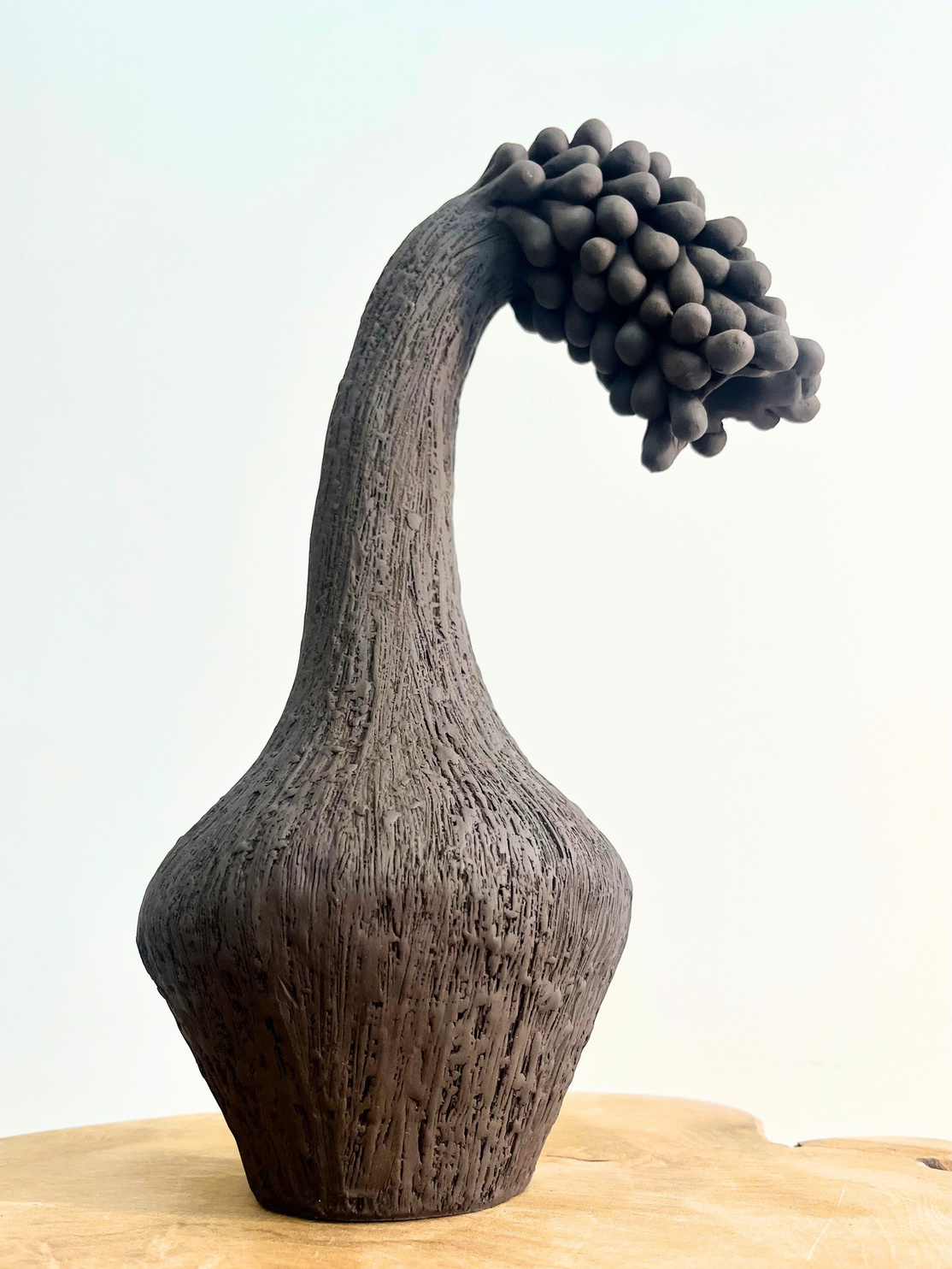 The gravity of sorrow sculpture, tall dark stoneware form with a curved neck bending under a dense cluster of rounded forms — view 2