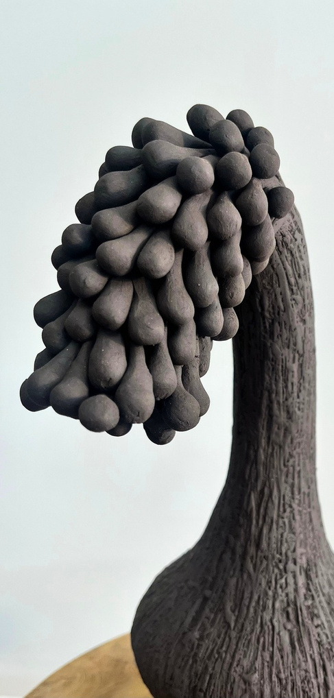 The gravity of sorrow sculpture, tall dark stoneware form with a curved neck bending under a dense cluster of rounded forms