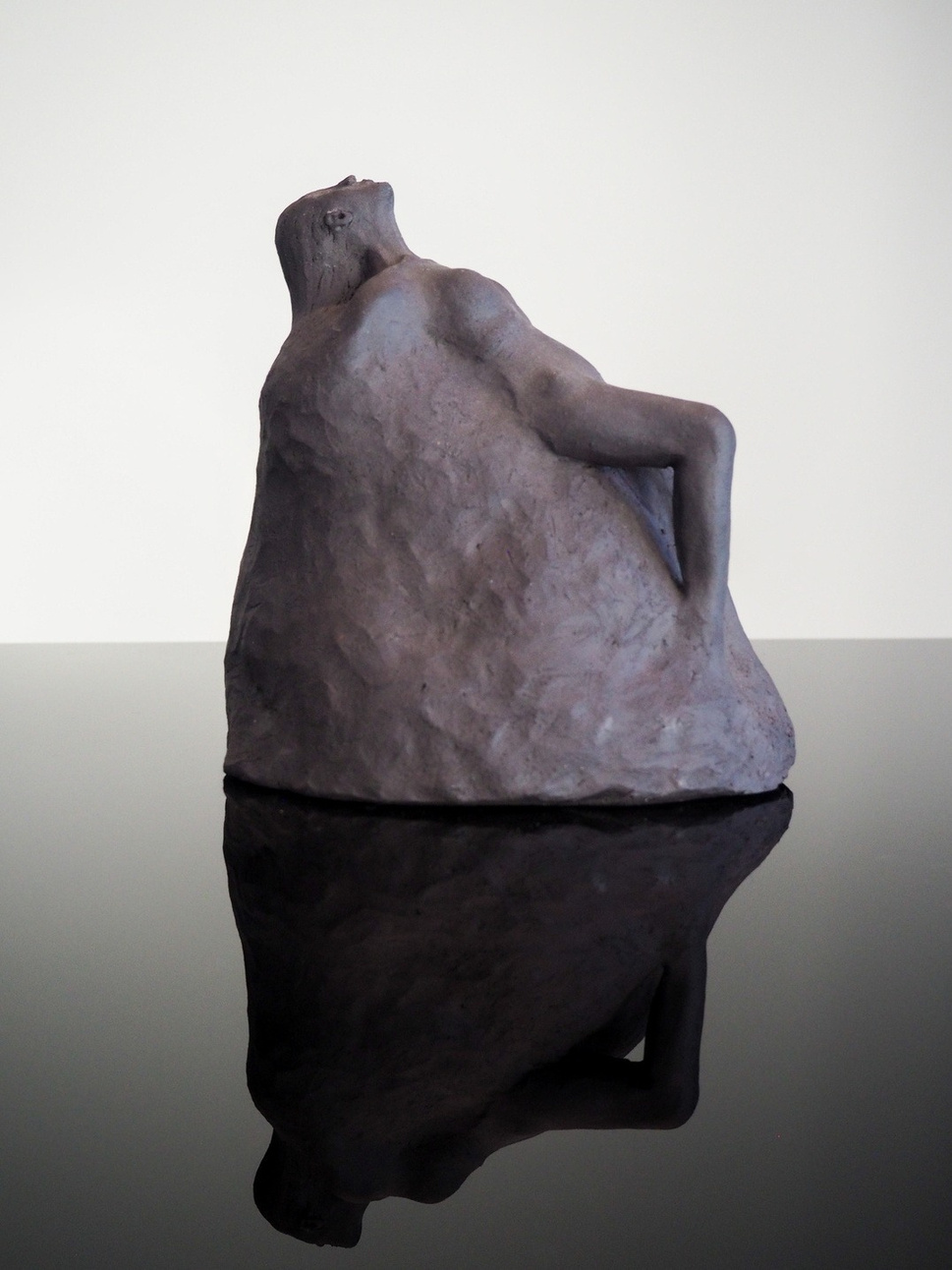 The rise sculpture, dark stoneware figure appearing to lift itself from or settle into a surface